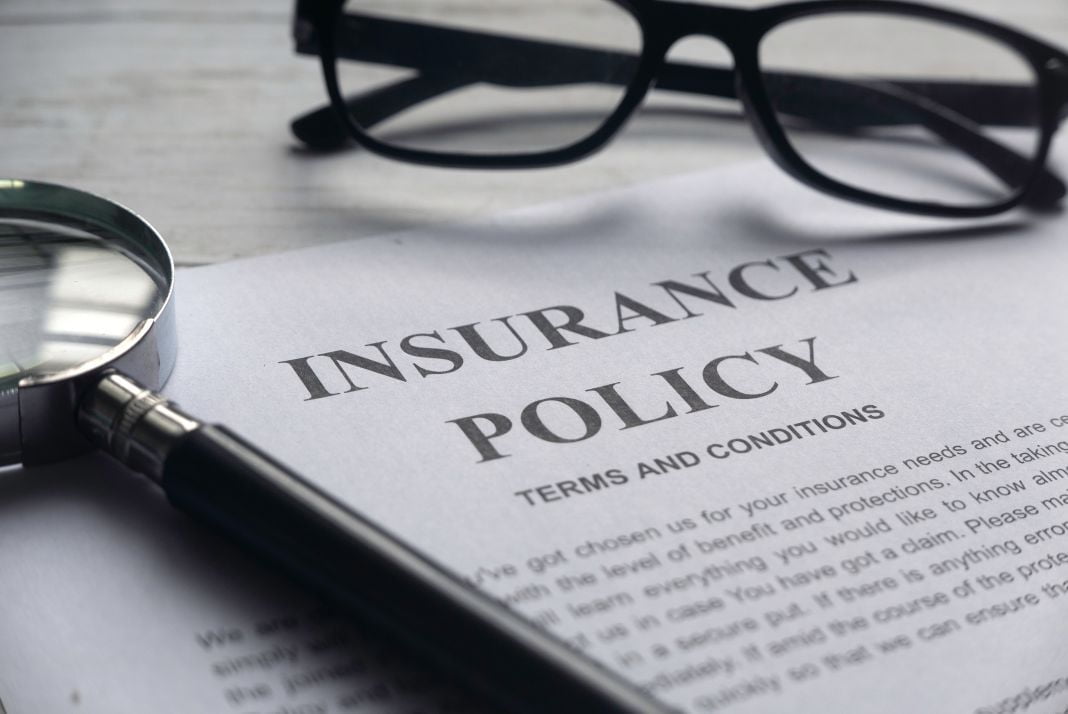 A paper for insurance policy terms and conditions with a magnifying glass and reading glasses sitting nearby.