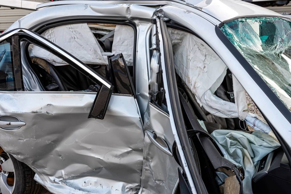 A car that has been in a bad accident. The door is crushed. The windshield is broken.