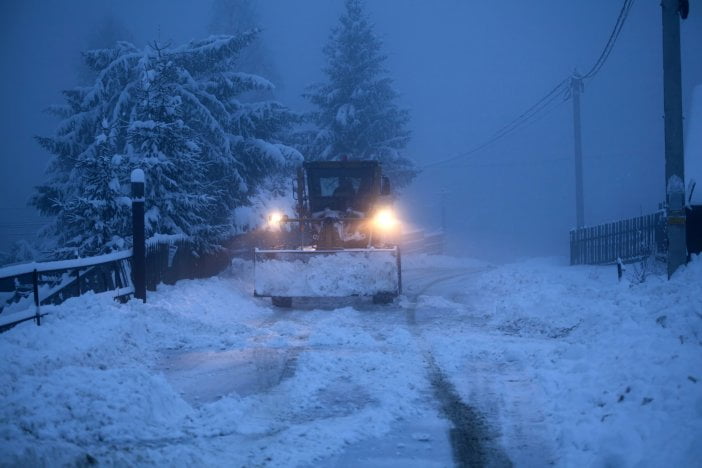 A tractor plowing a snowy road during a snowstorm