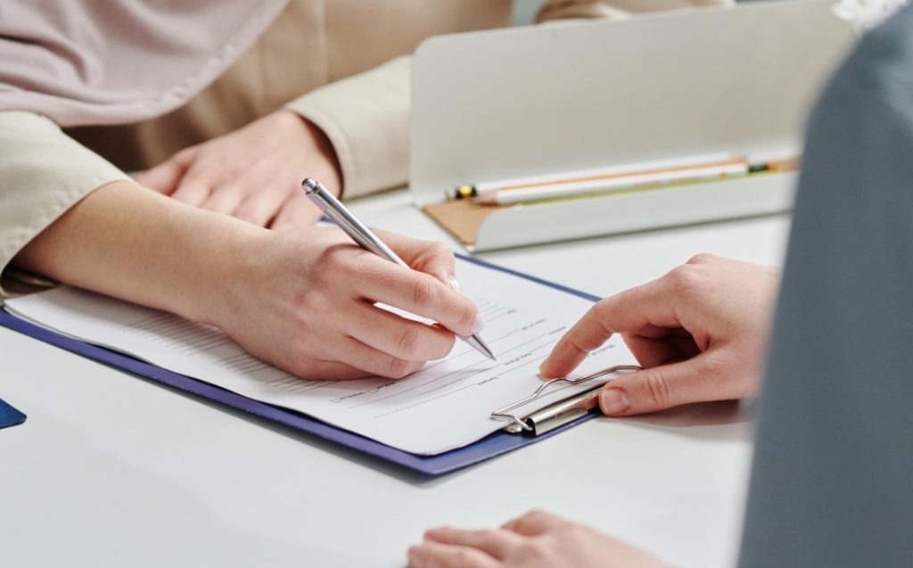 A woman completing a form with another person guiding her