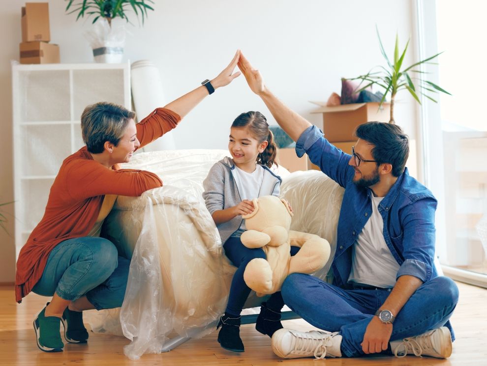 A mother and father. standing on each side of their daughter with their arms. making the shape of a home roof over their daughter's head. It appears similar to giving a high five