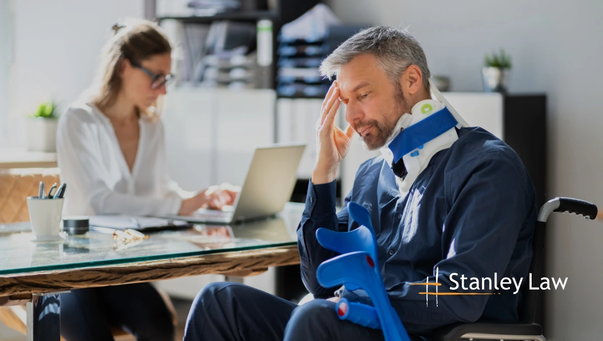 Injured worker in a neck brace and wheelchair consulting with an office worker, highlighting workers' compensation support.